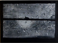 An abstract square artwork depicting a dark gray textured surface covered with scattered raindrops, divided horizontally by a thick black band, with a small dark bird silhouette near the center.